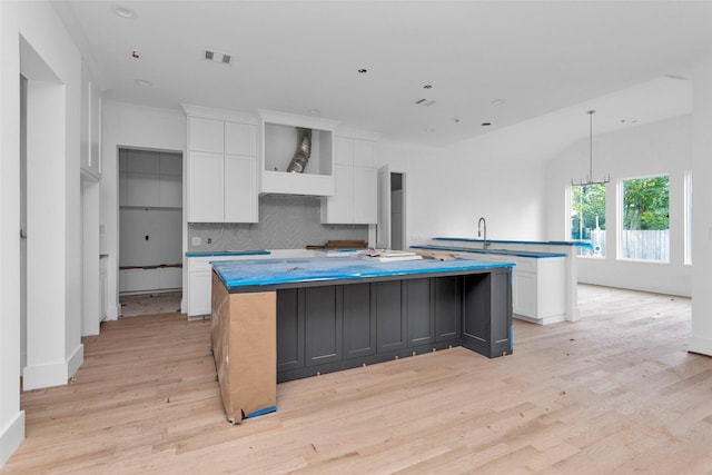 kitchen with white cabinets, light wood-type flooring, an island with sink, tasteful backsplash, and decorative light fixtures