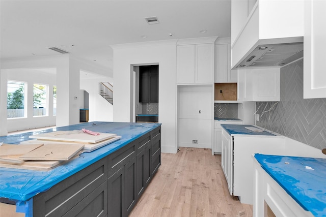 kitchen featuring white cabinetry, premium range hood, backsplash, crown molding, and light wood-type flooring