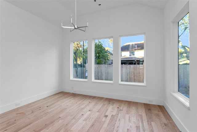 unfurnished room featuring light hardwood / wood-style floors, lofted ceiling, and an inviting chandelier