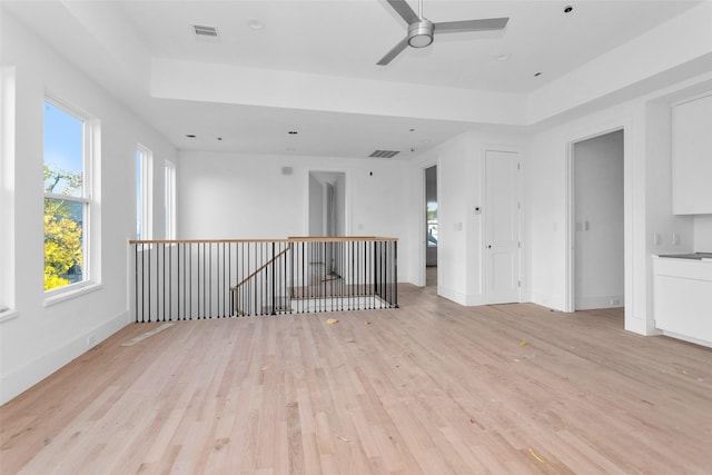 spare room featuring a raised ceiling, ceiling fan, and light hardwood / wood-style flooring