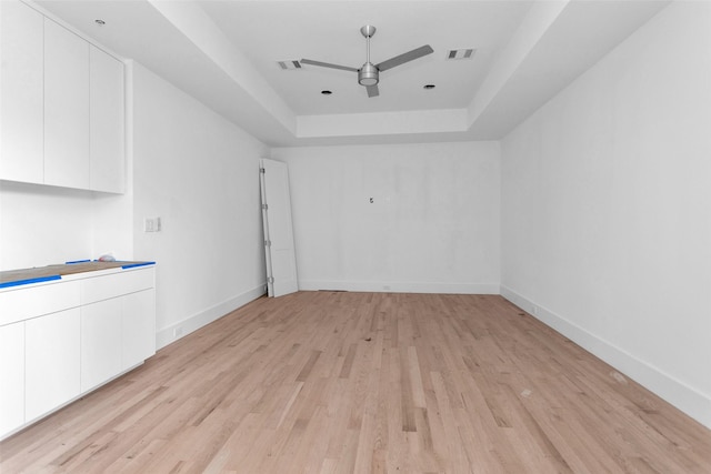 interior space featuring ceiling fan, a raised ceiling, and light wood-type flooring