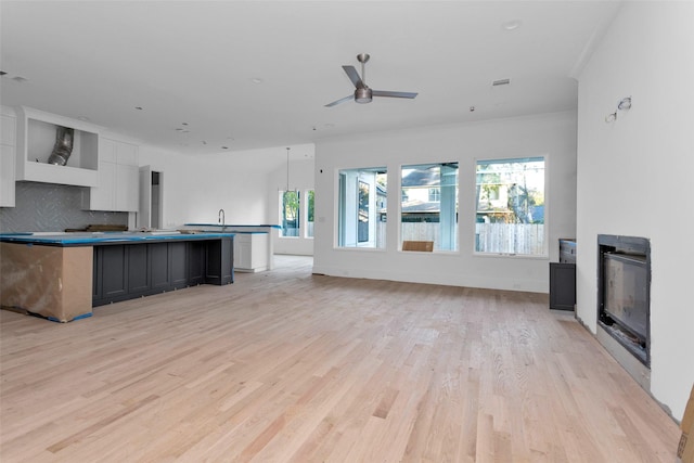 kitchen with backsplash, ornamental molding, light hardwood / wood-style floors, white cabinetry, and an island with sink