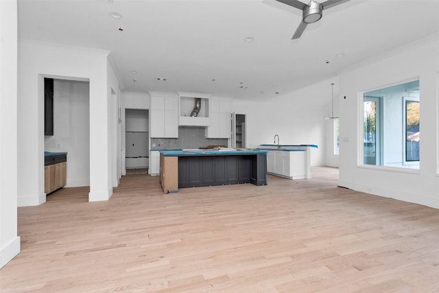 kitchen featuring ceiling fan, tasteful backsplash, light hardwood / wood-style flooring, a kitchen island with sink, and white cabinets