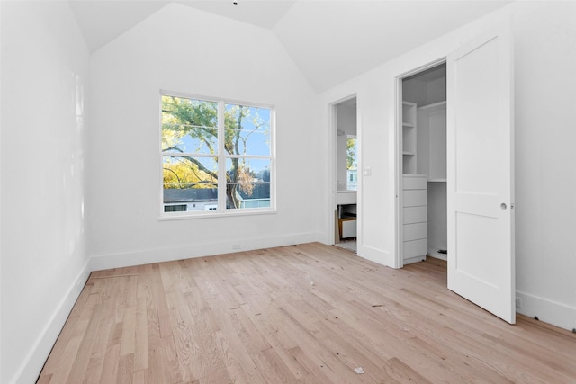 unfurnished bedroom featuring a walk in closet, light wood-type flooring, and vaulted ceiling