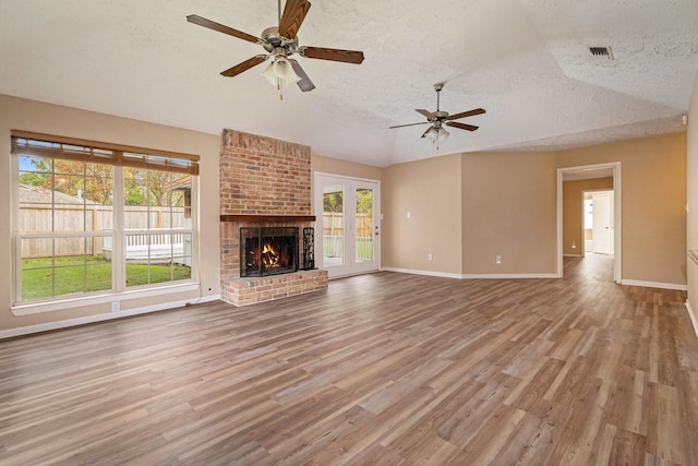 unfurnished living room featuring a fireplace, light wood-type flooring, a textured ceiling, and vaulted ceiling