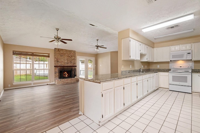 kitchen featuring white appliances, stone counters, light hardwood / wood-style flooring, a textured ceiling, and kitchen peninsula