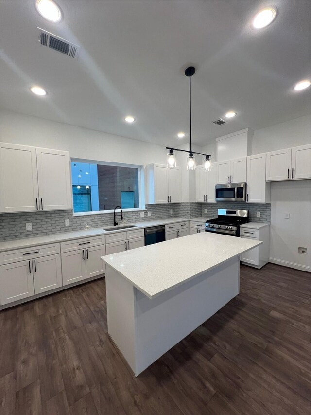 kitchen with appliances with stainless steel finishes, sink, pendant lighting, a center island, and white cabinetry