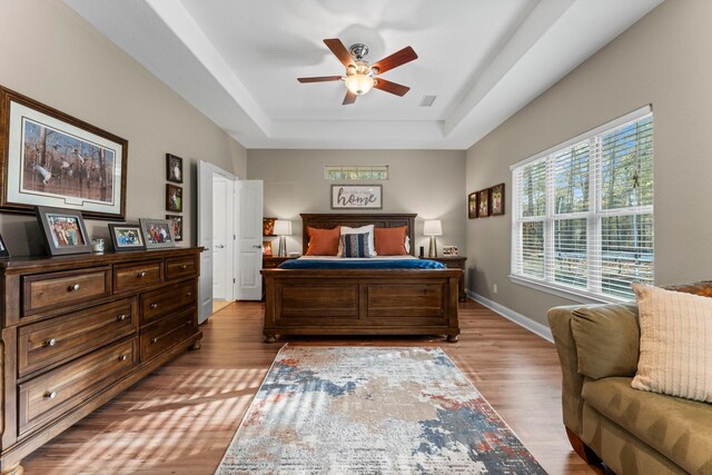 bedroom with a raised ceiling, ceiling fan, and light hardwood / wood-style floors