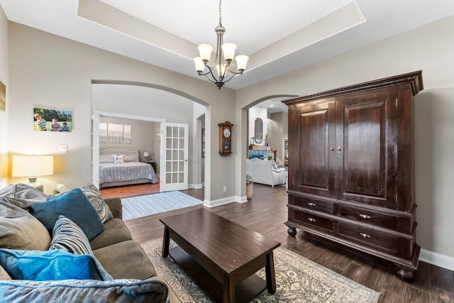 living room with a notable chandelier, dark hardwood / wood-style flooring, and a raised ceiling