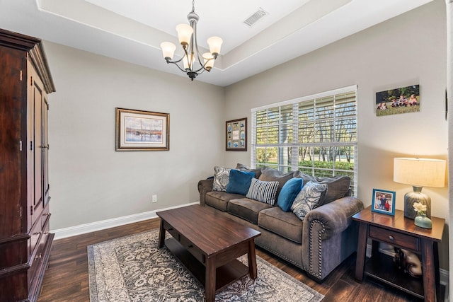 living room featuring a raised ceiling, dark hardwood / wood-style flooring, and a chandelier