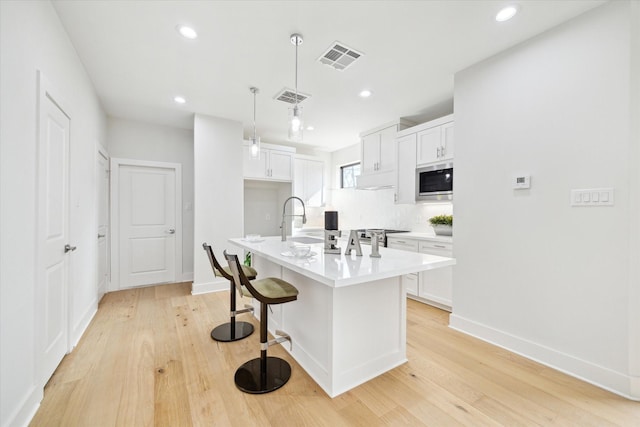 kitchen with light wood-style floors, white cabinets, stainless steel microwave, and visible vents