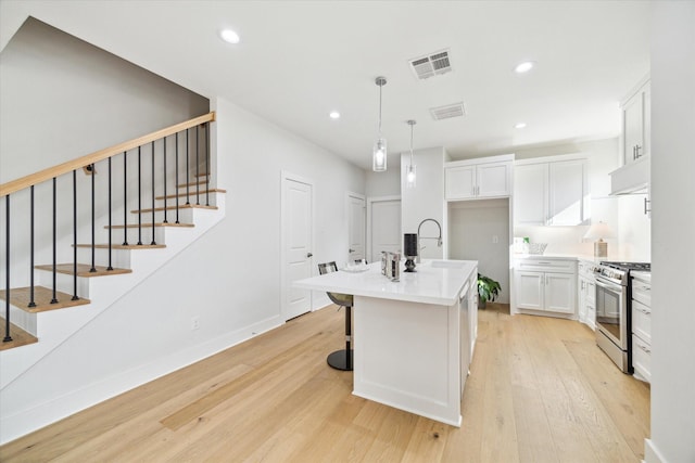 kitchen featuring visible vents, light wood-style flooring, white cabinets, gas range, and under cabinet range hood