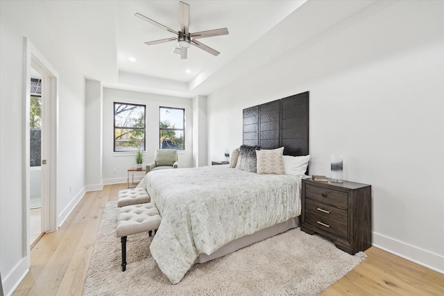 bedroom with light wood-style flooring, baseboards, a raised ceiling, and recessed lighting