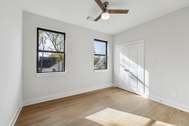 spare room with light wood finished floors, baseboards, visible vents, and a ceiling fan