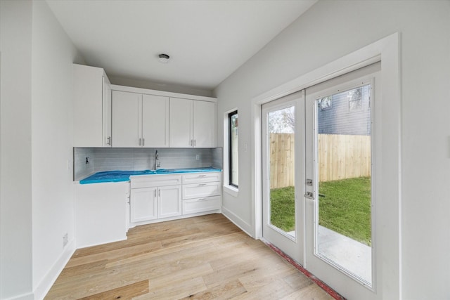 kitchen with french doors, light wood finished floors, backsplash, white cabinetry, and a sink