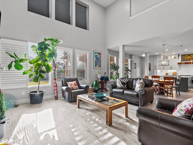 living room with an inviting chandelier, a towering ceiling, and light hardwood / wood-style flooring