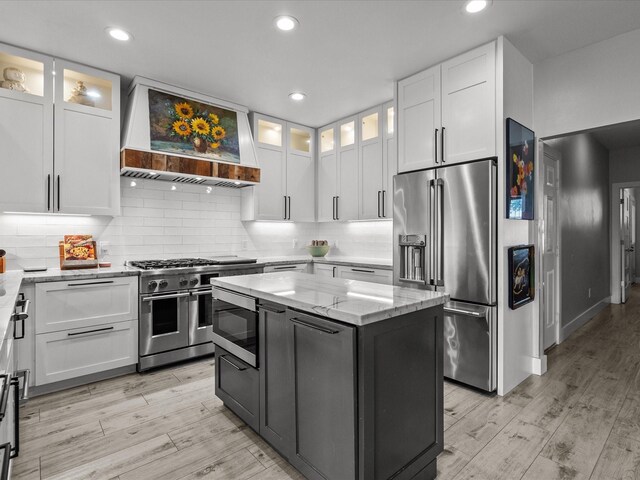 kitchen with custom exhaust hood, a center island, high end appliances, white cabinets, and light wood-type flooring