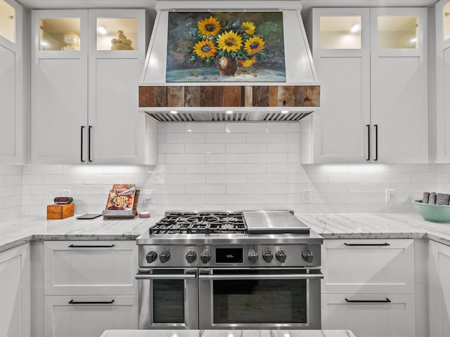 kitchen with decorative backsplash, white cabinetry, extractor fan, and range with two ovens