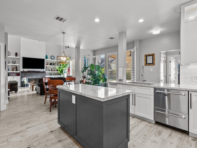 kitchen featuring sink, light hardwood / wood-style flooring, white cabinets, a center island, and a tiled fireplace