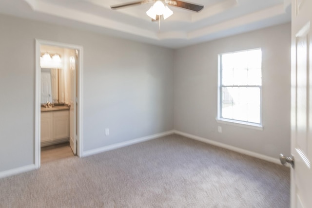 unfurnished bedroom with sink, ensuite bath, ceiling fan, a tray ceiling, and light colored carpet