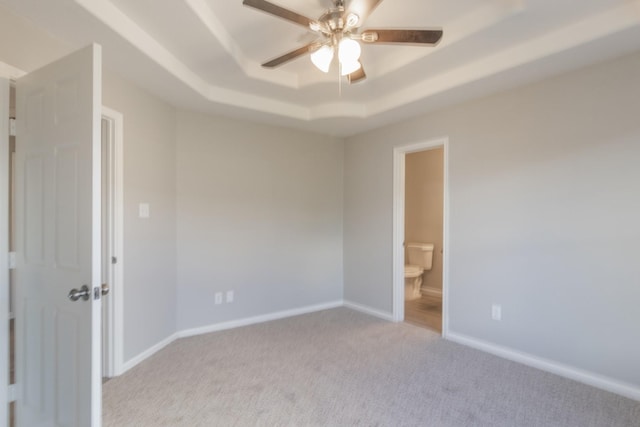 unfurnished bedroom featuring light carpet, connected bathroom, a tray ceiling, and ceiling fan