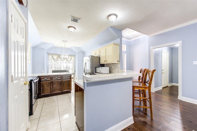 kitchen featuring pendant lighting, light wood-type flooring, appliances with stainless steel finishes, cream cabinetry, and a breakfast bar area