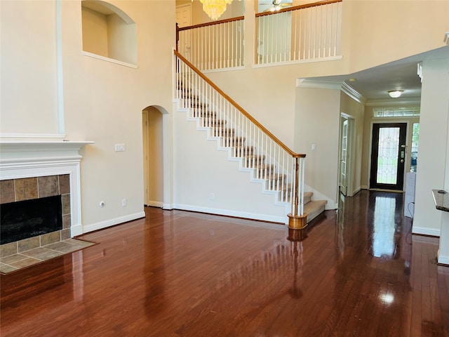 unfurnished living room with a high ceiling, ceiling fan, ornamental molding, dark hardwood / wood-style flooring, and a tiled fireplace