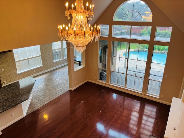 unfurnished dining area with dark hardwood / wood-style flooring, an inviting chandelier, and high vaulted ceiling