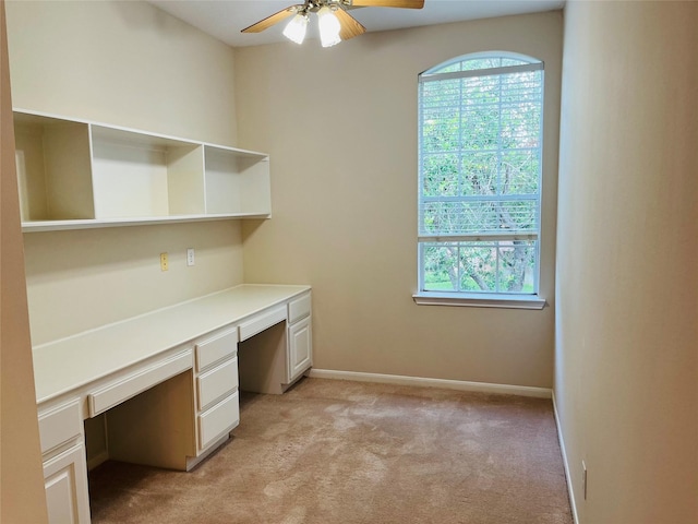 unfurnished office featuring ceiling fan, light colored carpet, and built in desk