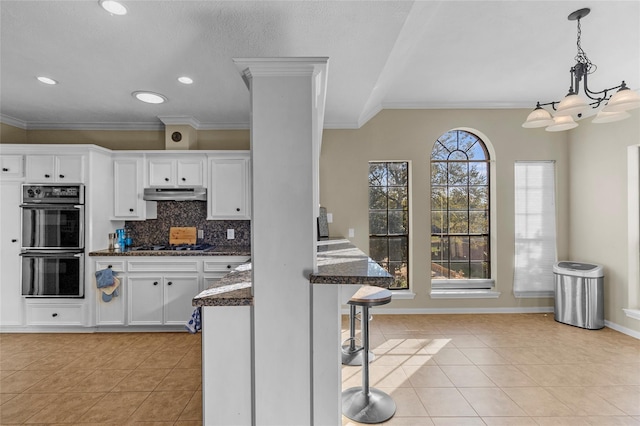 kitchen featuring a kitchen bar, white cabinetry, decorative backsplash, light tile patterned floors, and multiple ovens