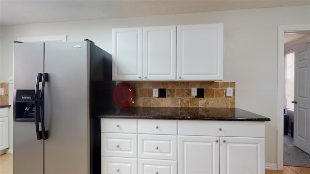 kitchen featuring stainless steel refrigerator with ice dispenser, backsplash, dark stone counters, light tile patterned floors, and white cabinetry