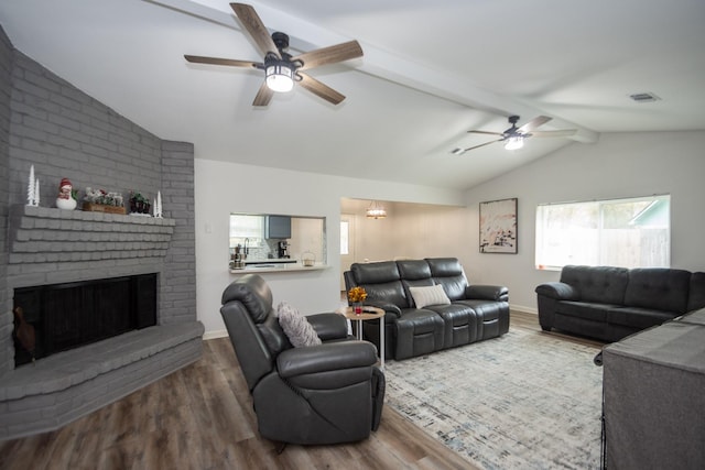 living room featuring hardwood / wood-style floors, lofted ceiling with beams, a brick fireplace, and ceiling fan