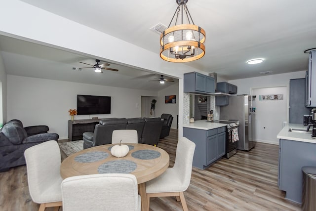 dining space featuring light hardwood / wood-style flooring, ceiling fan with notable chandelier, and sink