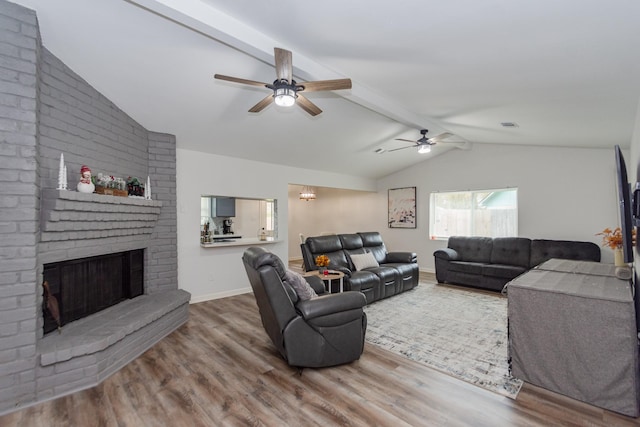 living room featuring hardwood / wood-style floors, lofted ceiling with beams, a brick fireplace, and ceiling fan