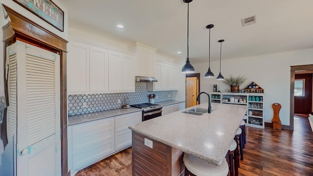 kitchen featuring white cabinets, gas range, dark hardwood / wood-style floors, an island with sink, and a kitchen bar