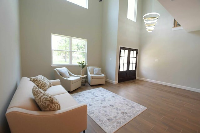 living room featuring a towering ceiling, hardwood / wood-style flooring, french doors, and a healthy amount of sunlight