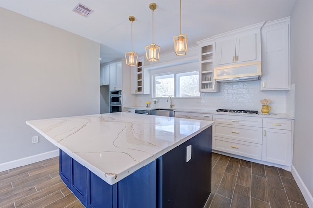 kitchen with light stone countertops, a kitchen island, white cabinetry, sink, and hanging light fixtures