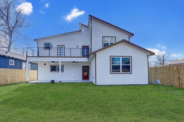 rear view of house with ceiling fan, a lawn, and a balcony