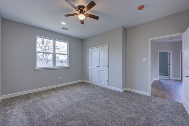 unfurnished bedroom with ceiling fan, a closet, and dark carpet