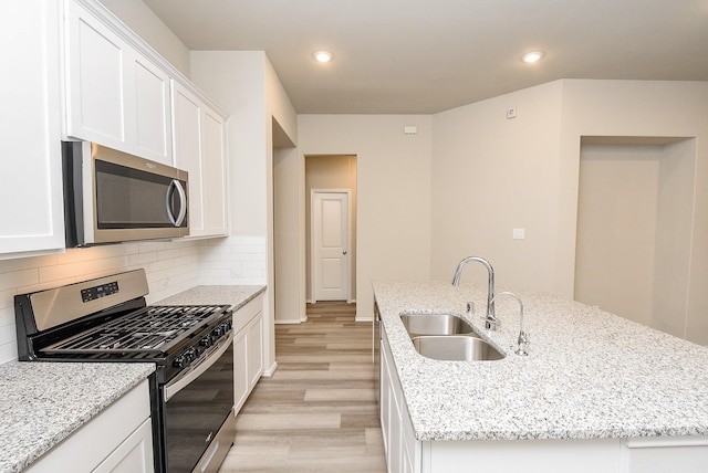 kitchen featuring light stone countertops, stainless steel appliances, sink, light hardwood / wood-style floors, and an island with sink