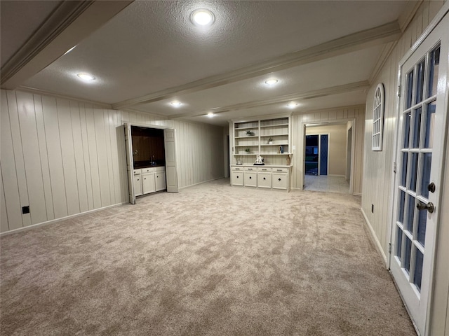 basement with wood walls, ornamental molding, a textured ceiling, built in features, and light colored carpet