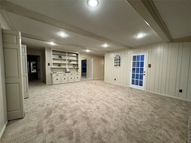 basement featuring a textured ceiling, light colored carpet, built in features, and wood walls