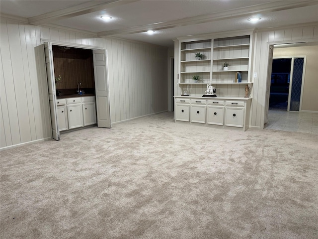 unfurnished living room featuring wood walls, sink, ornamental molding, and light carpet