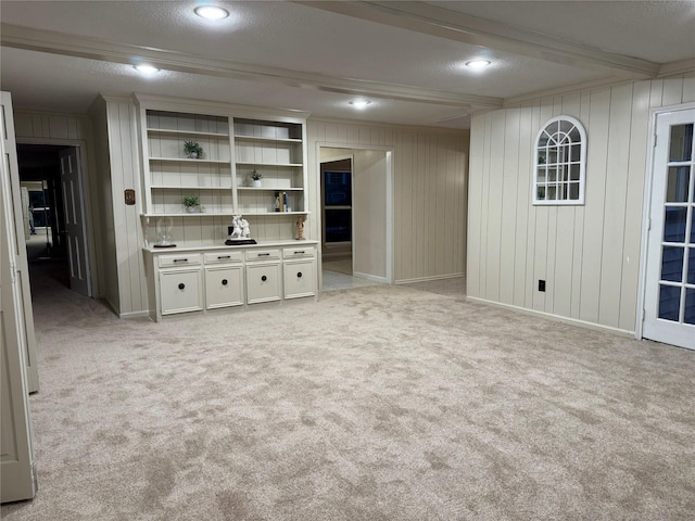 unfurnished living room featuring light carpet, a textured ceiling, crown molding, and wooden walls