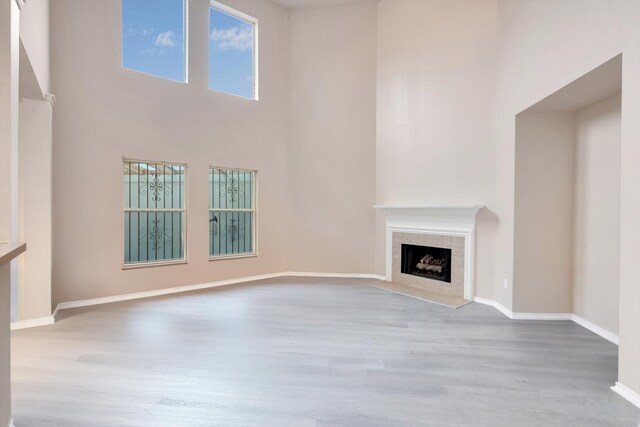 unfurnished living room with a tiled fireplace, light hardwood / wood-style floors, and a high ceiling