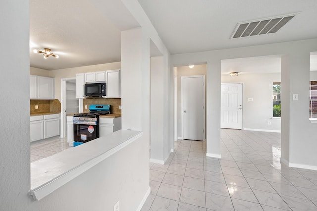 kitchen featuring decorative backsplash, light tile patterned floors, stainless steel gas stove, and white cabinetry