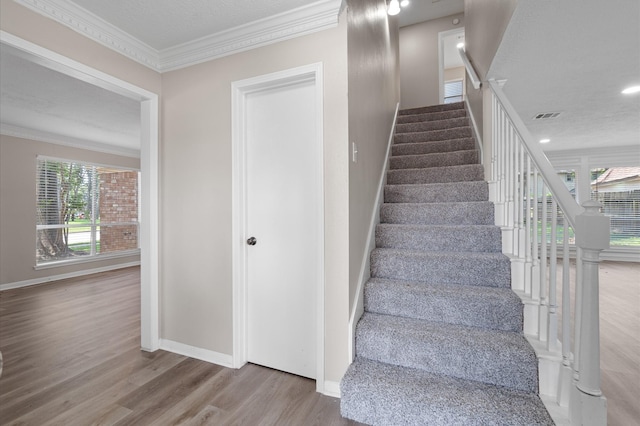 stairway featuring hardwood / wood-style flooring, ornamental molding, and a textured ceiling