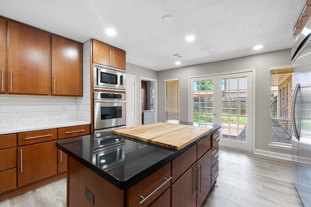 kitchen featuring appliances with stainless steel finishes, a textured ceiling, light hardwood / wood-style floors, and a kitchen island