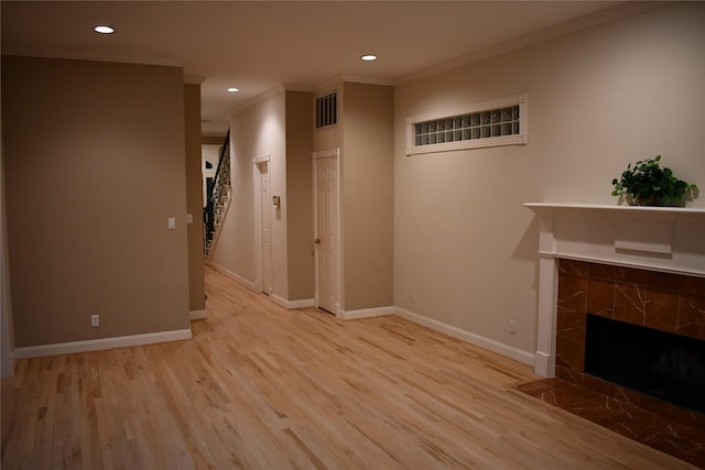 unfurnished living room with a tiled fireplace, light hardwood / wood-style floors, and ornamental molding