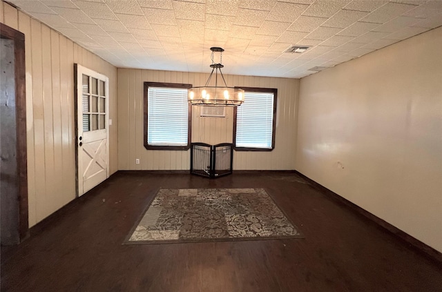 unfurnished dining area featuring wooden walls, dark hardwood / wood-style floors, and a notable chandelier